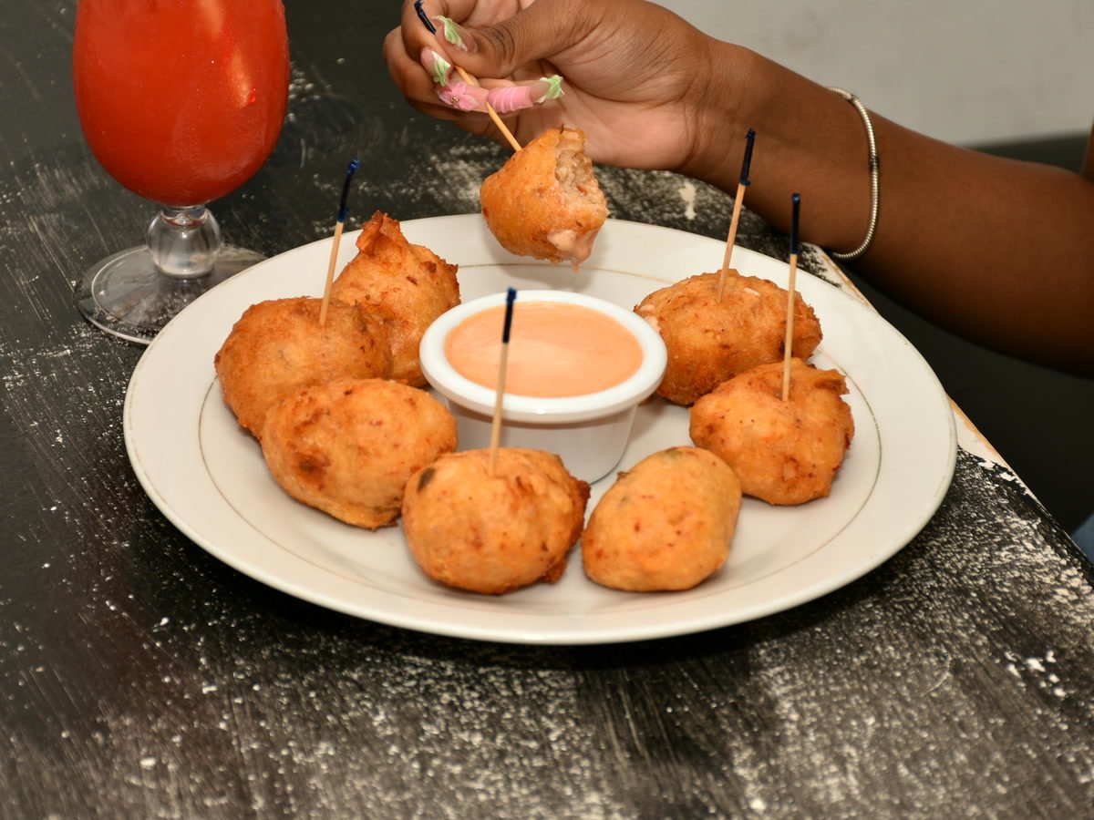 Golden fried conch fritters on picks around a bowl of house fritter sauce.