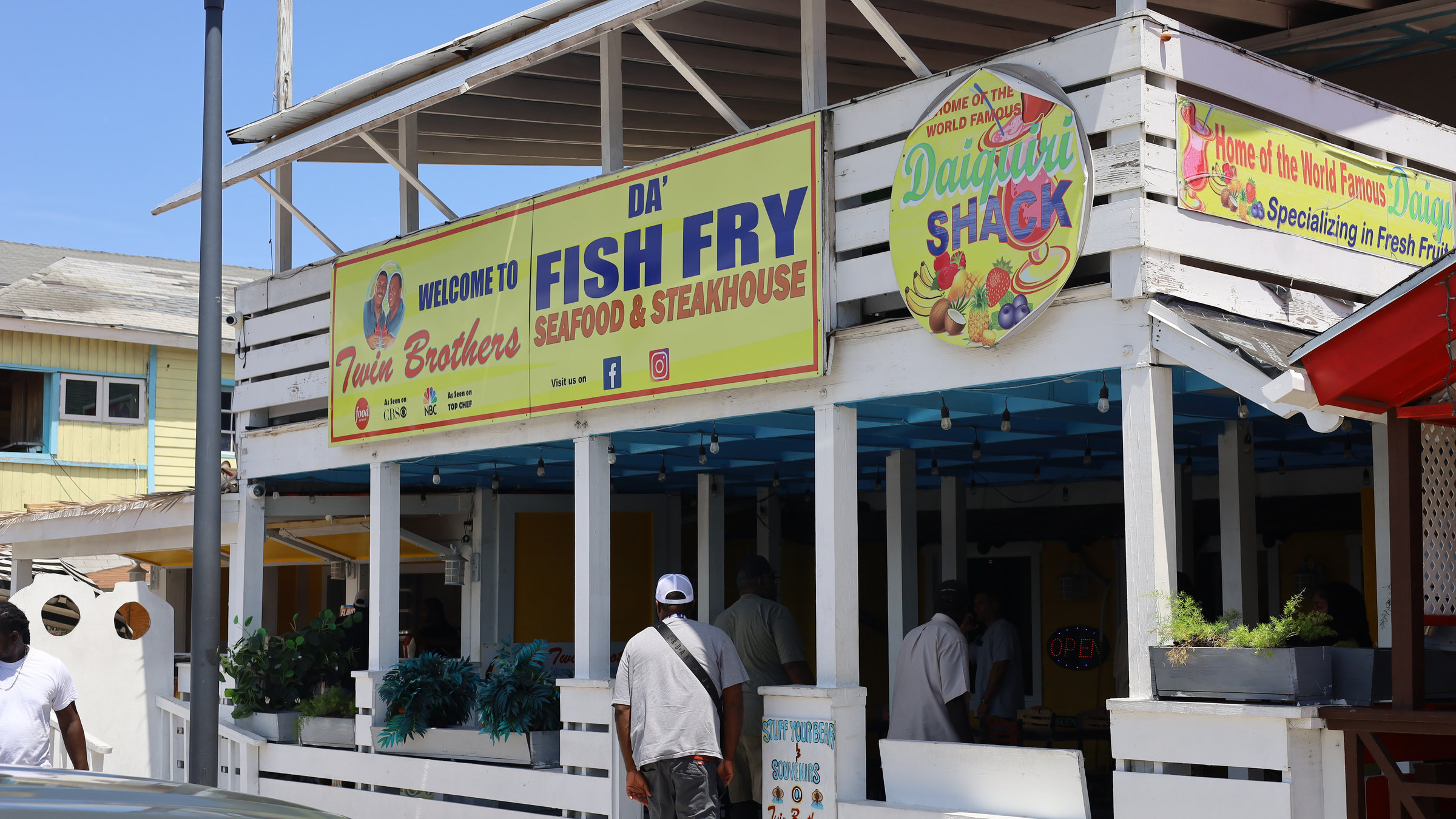 The Twin Brothers frontage at the Fish Fry, Arawak Cay, with guests walking in under the sign.