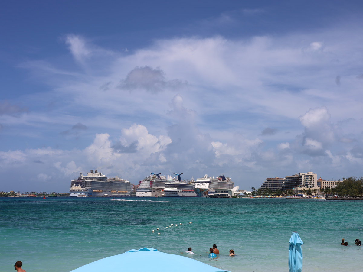 Turquoise water and swimmers off Arawak Cay, with cruise ships docked across the harbour.