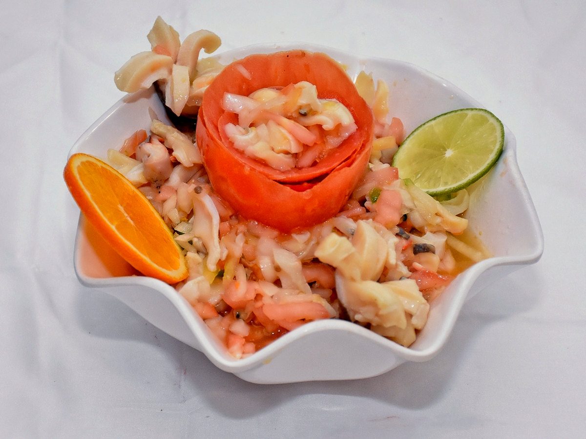 Fresh Bahamian conch salad in a white scalloped bowl, topped with a tomato rose, with orange and lime, at Twin Brothers on Arawak Cay.