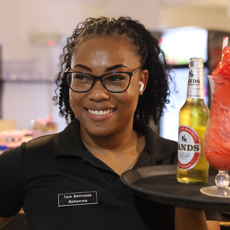 A Twin Brothers server carrying a tray with a cold beer and a frozen strawberry daiquiri.