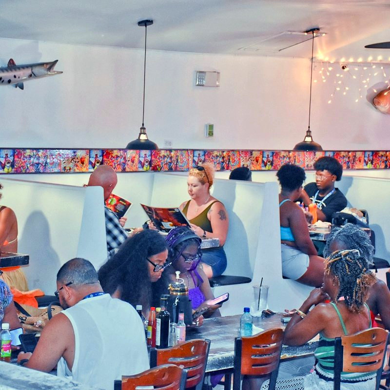 A full dining room at Twin Brothers, guests in white booths under a row of painted art panels.