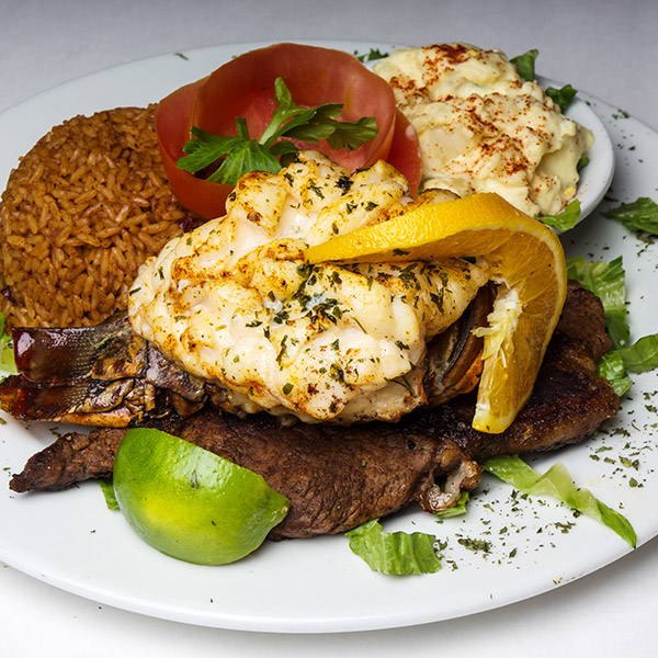 Grilled steak topped with lobster, with peas and rice and potato salad