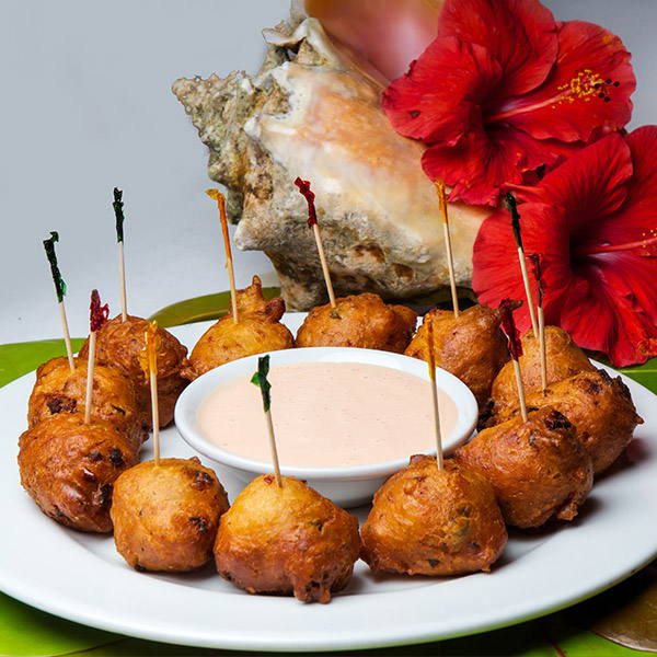 Golden conch fritters ringed around a bowl of house fritter sauce