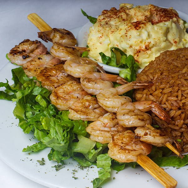 Grilled shrimp skewers with potato salad and peas and rice